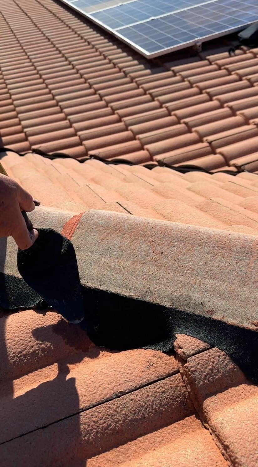 Man lifting part of a roof’s underlayment, showing tile roof, with solar panels in background.