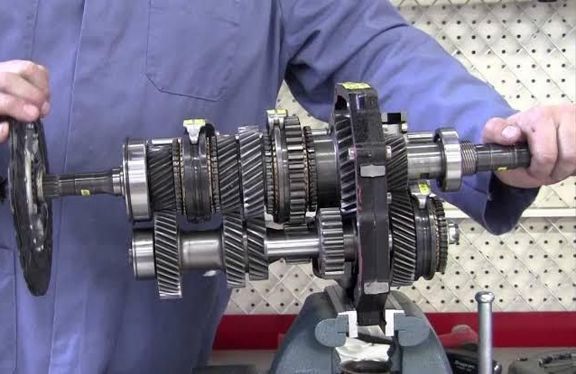 Mechanic holding a disassembled transmission with multiple gears on a workbench.
