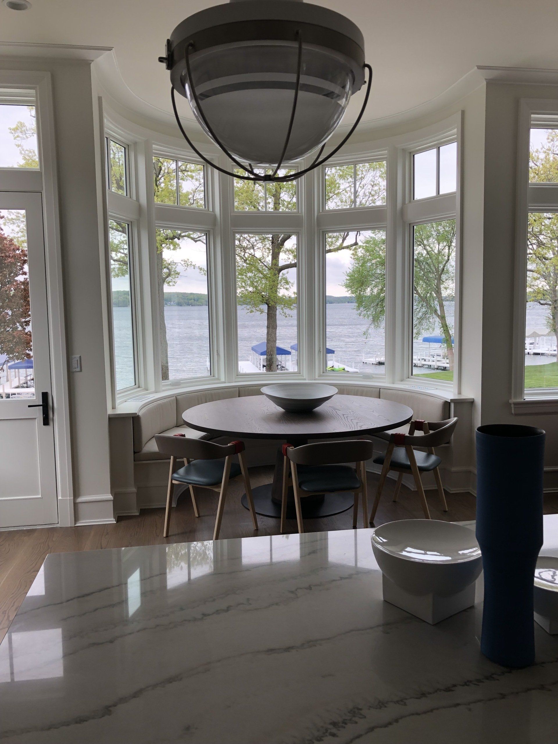 A dining room with a table and chairs and a large window overlooking a lake.