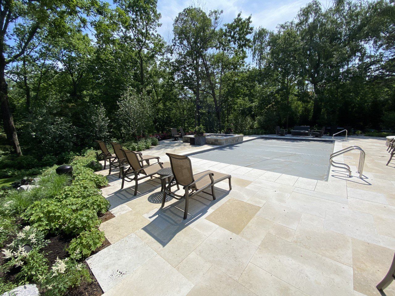 A patio with chairs and a table next to a swimming pool surrounded by trees.