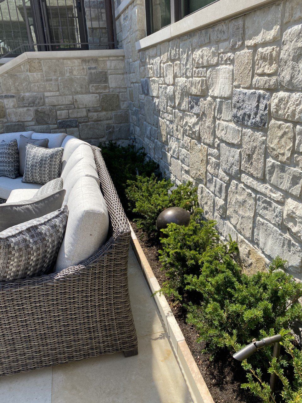 A wicker couch is sitting next to a stone wall.