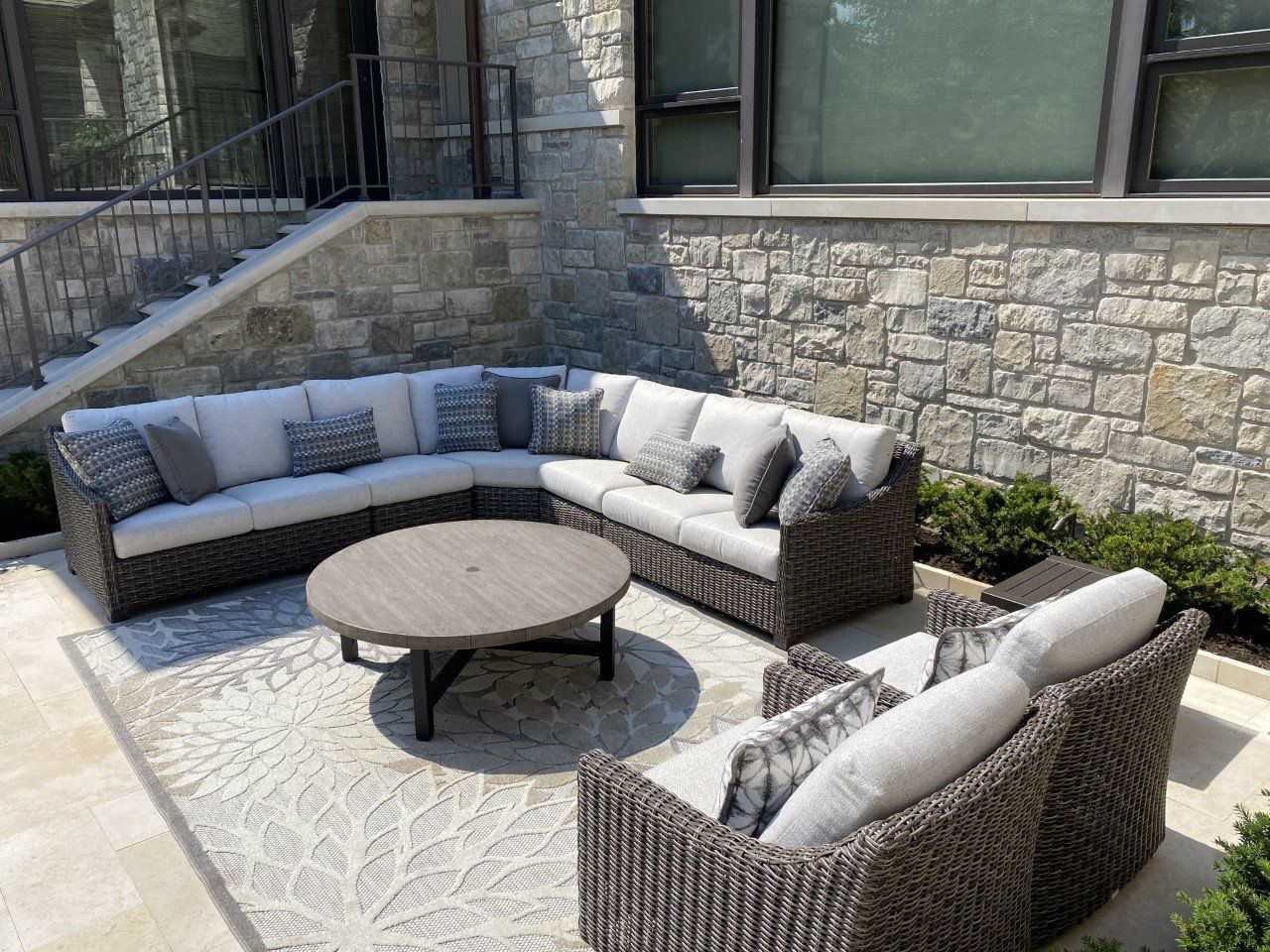 A patio with wicker furniture and a round table in front of a stone wall.
