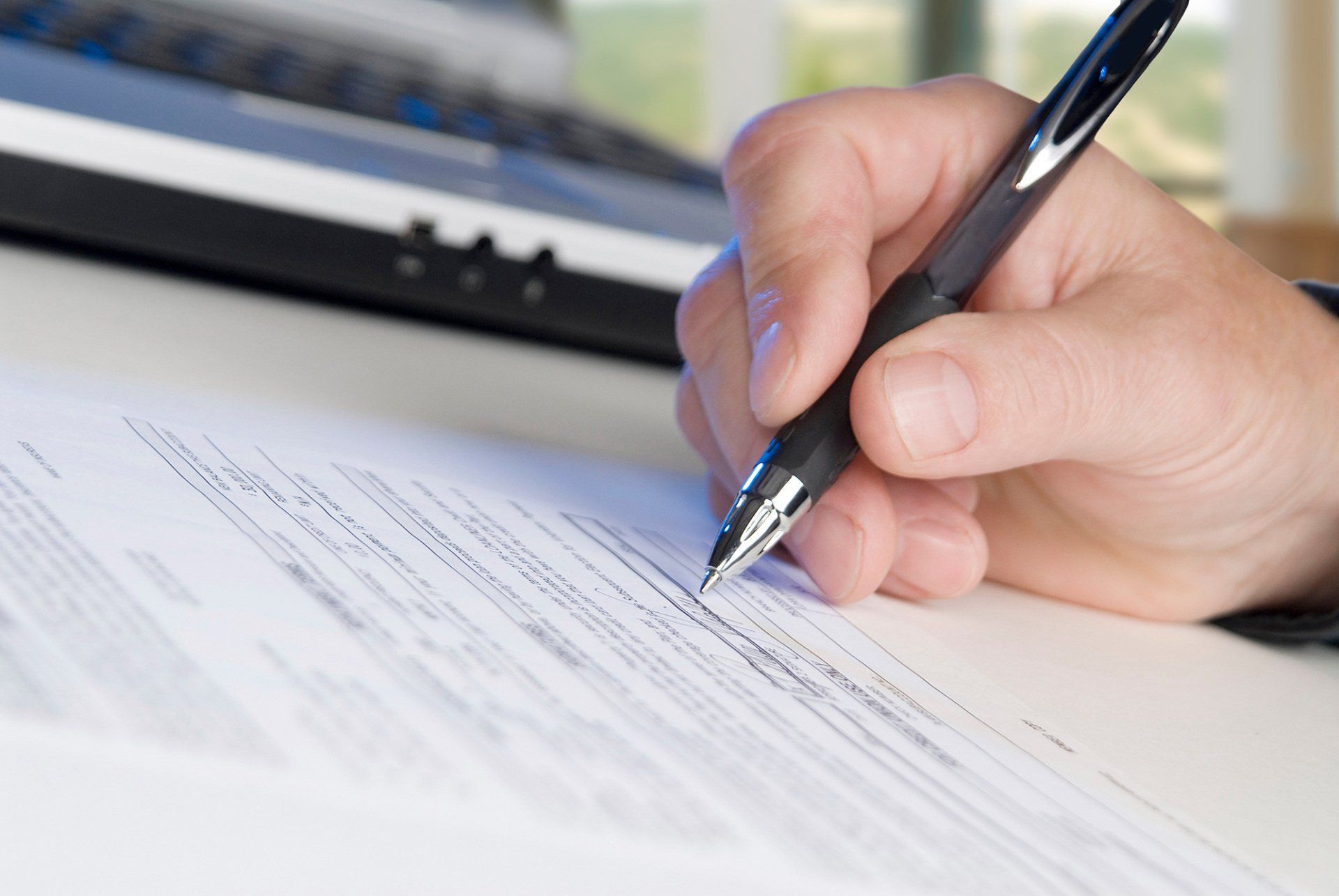 man signing papers, laptop, office windows in background