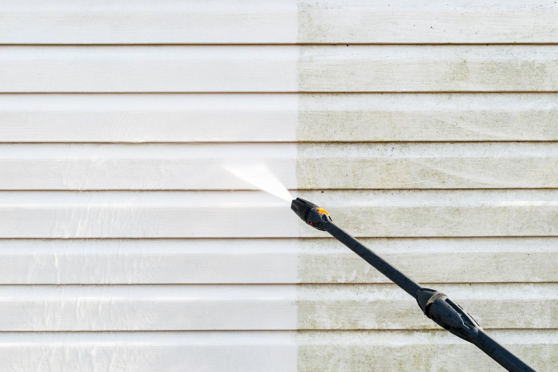 Power washer cleaning dirty siding, revealing a clean white surface.