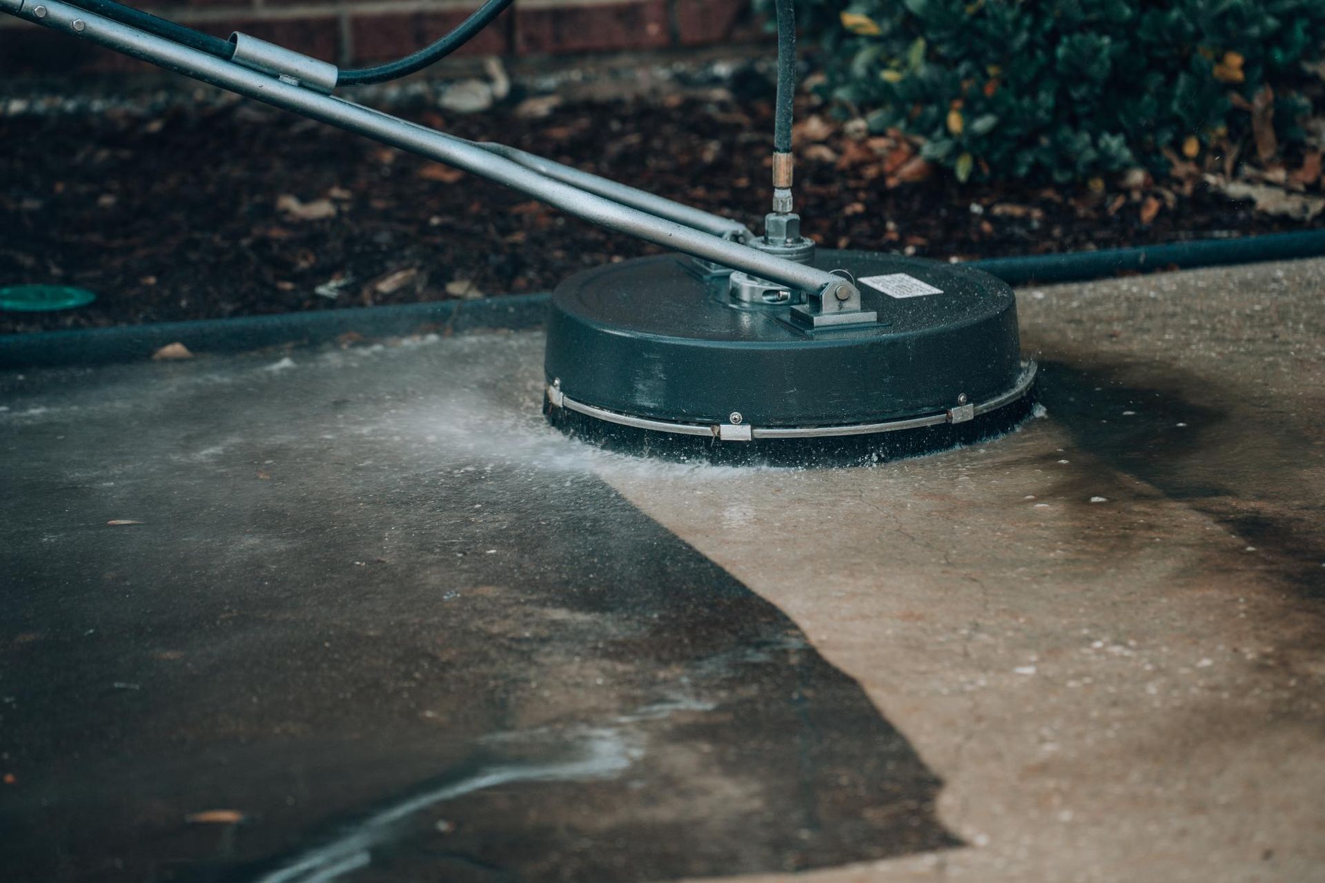 A concrete surface being cleaned with a circular power washer; spray and water are visible.