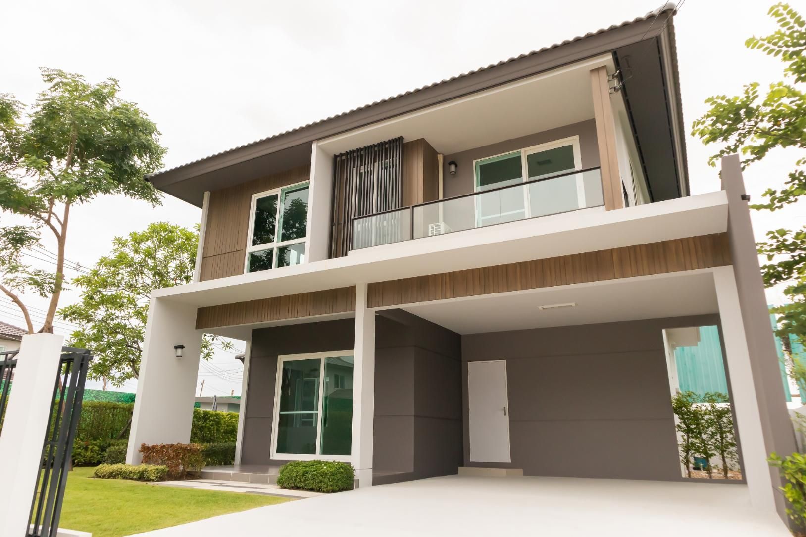 Two-story modern house with gray and white facade, carport, and glass balconies.
