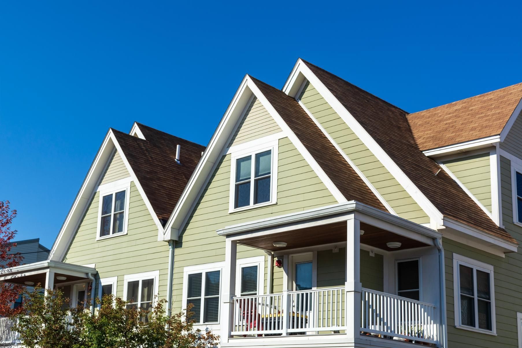 Green houses with brown roofs and white trim against a blue sky. 