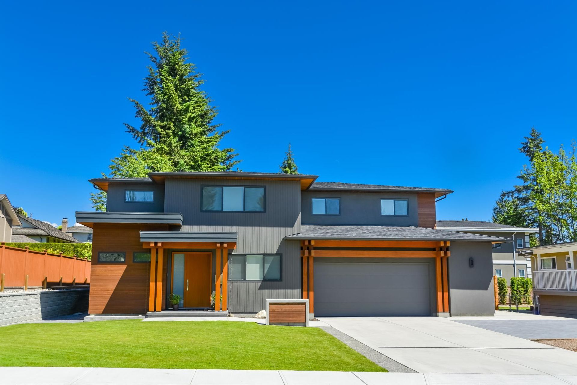 Modern two-story house with a gray exterior, wooden accents, and a two-car garage. 