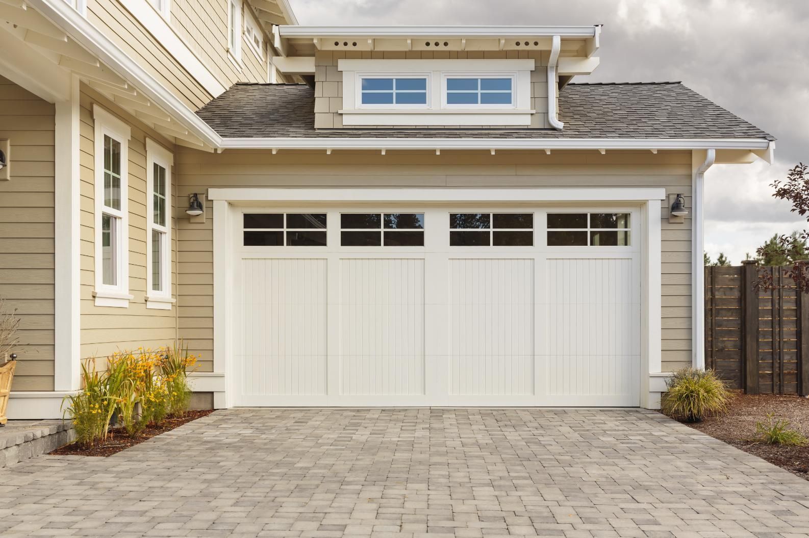 White garage door on a beige house with a brick driveway, under a cloudy sky.