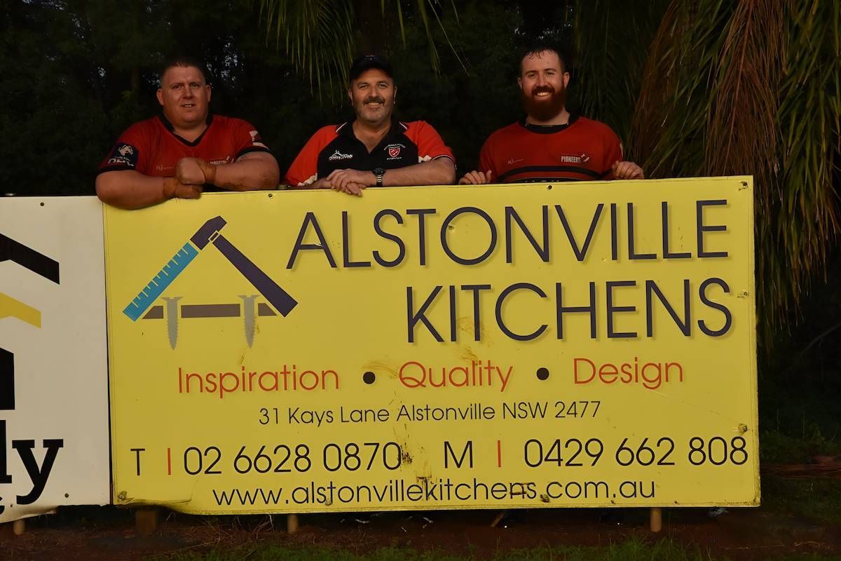 Four Men Standing Next To A Yellow Sign That Says Alstonville Kitchens — Alstonville Kitchens In Alstonville, NSW