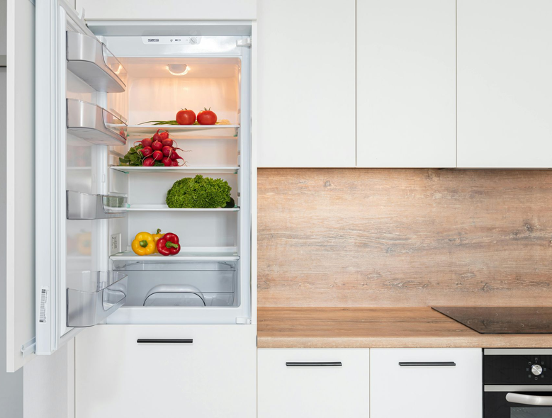 Open refrigerator with fresh produce in a white kitchen.