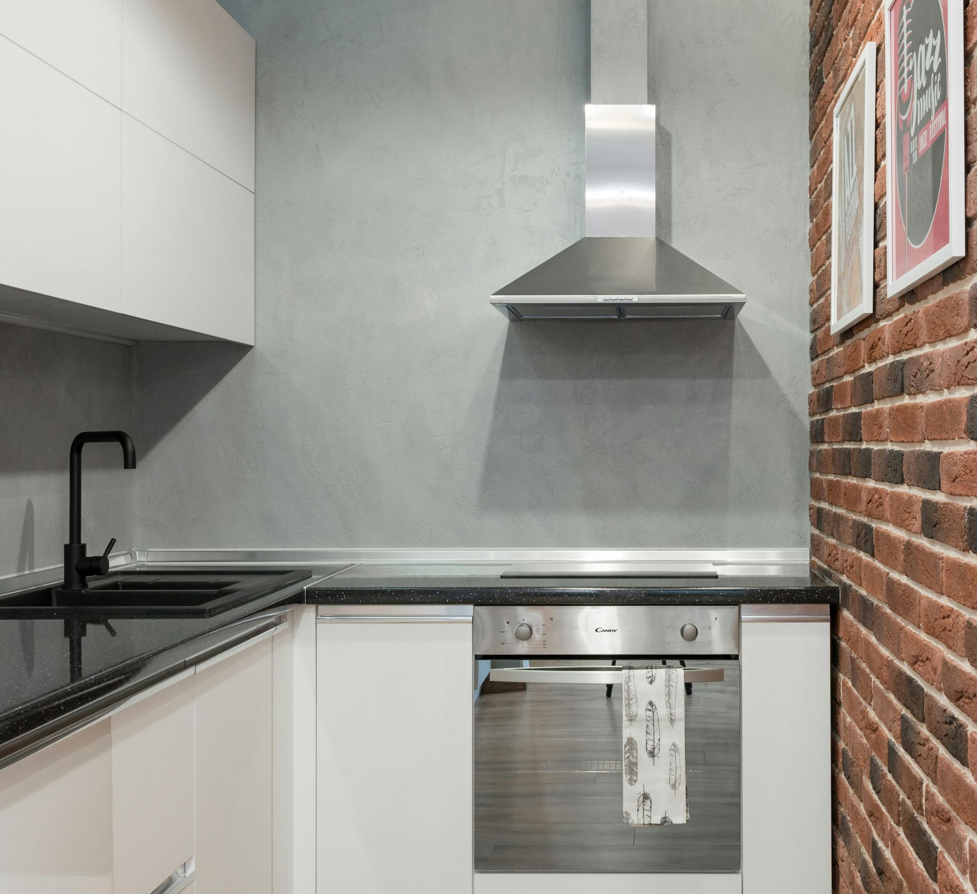 Modern kitchen with white cabinets, black countertop, brick wall, and stainless steel range hood.