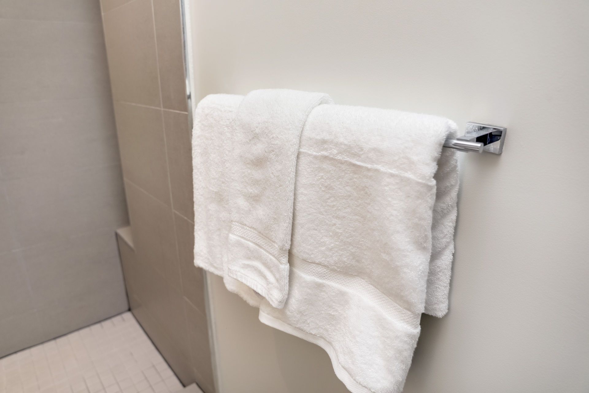 White towels on a chrome towel bar against a light wall in a bathroom.