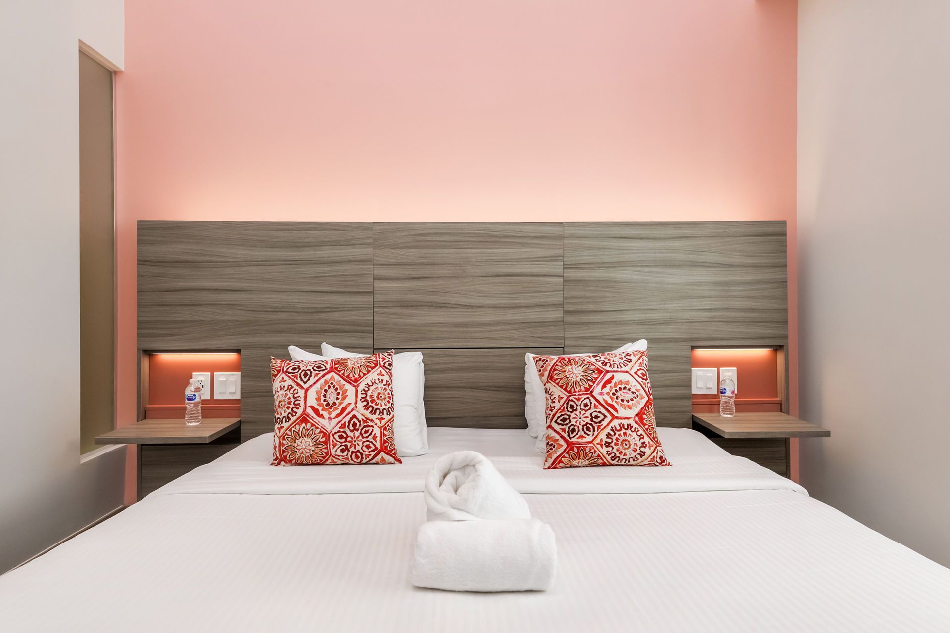 Bedroom with a bed, coral accent pillows, and gray headboard against a pink wall.
