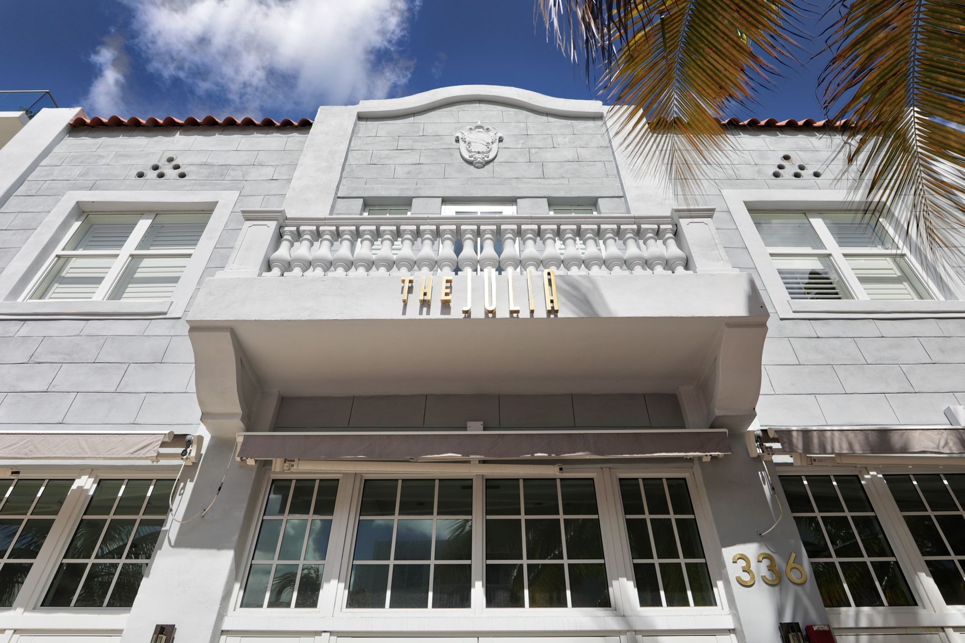 Gray and white Art Deco building facade with balcony and windows under blue sky.