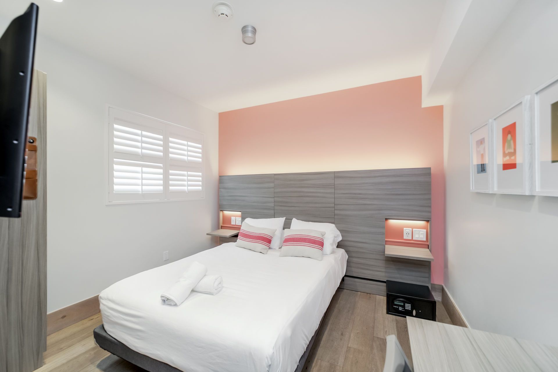 A bedroom with a double bed featuring white bedding, a gray headboard, peach-colored accent wall, and wood-style flooring.