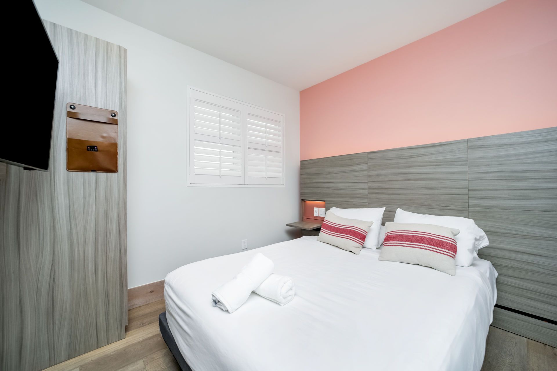Bedroom with bed, white bedding, pink wall, and wooden headboard.