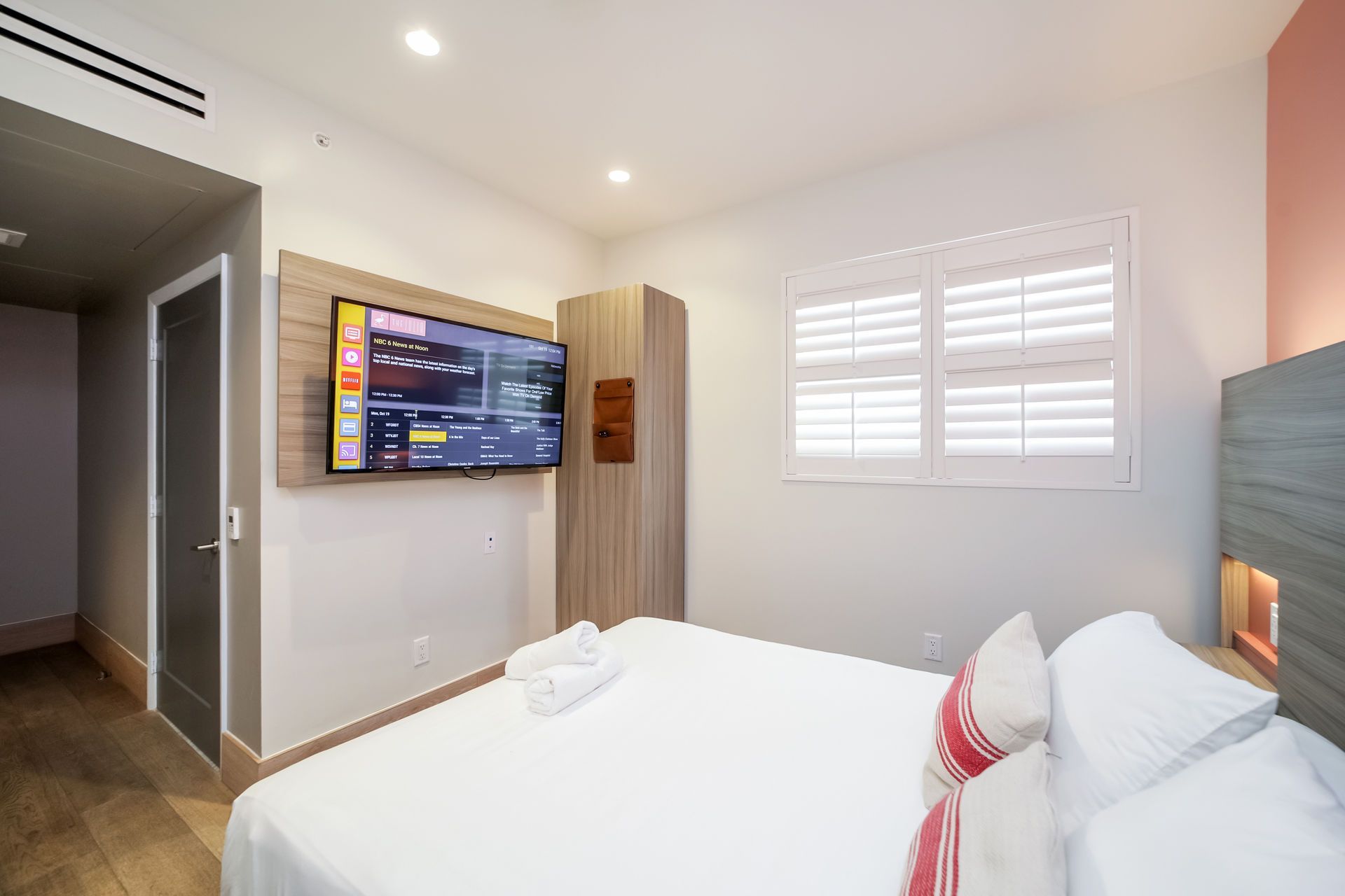 Bedroom with bed, TV on wall, closet, window with shutters.