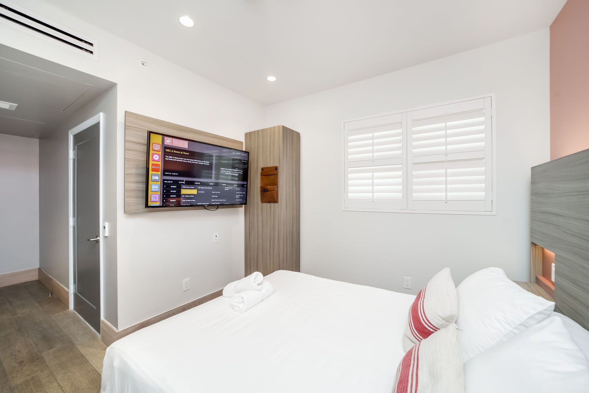 Bedroom with bed, TV on wall, closet, and window with shutters.