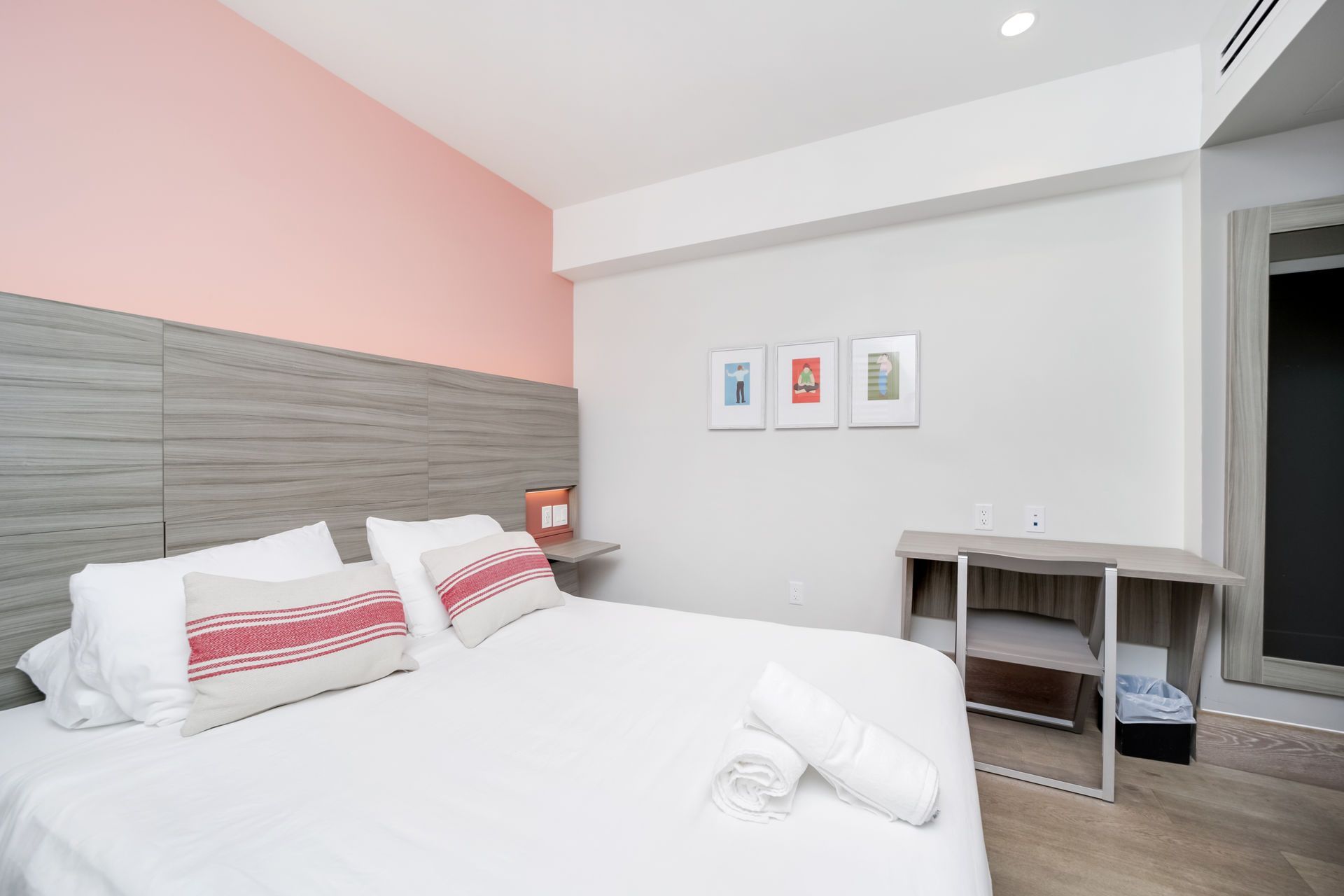 Bedroom with a bed, pillows, and artwork on the wall. Pink and gray color scheme.