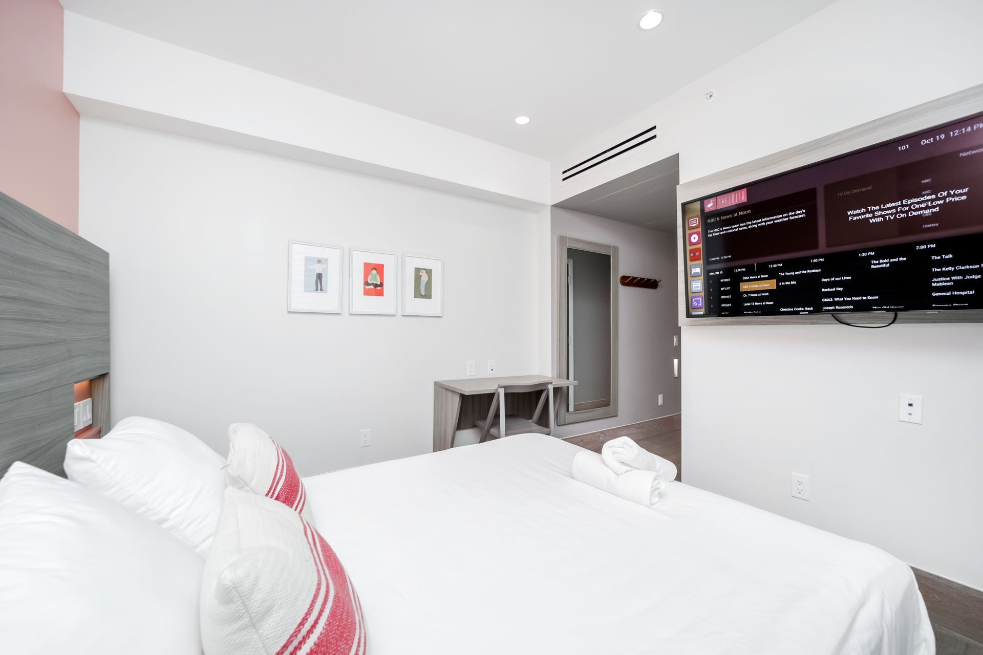Bedroom with white bed, TV on wall, and small desk.
