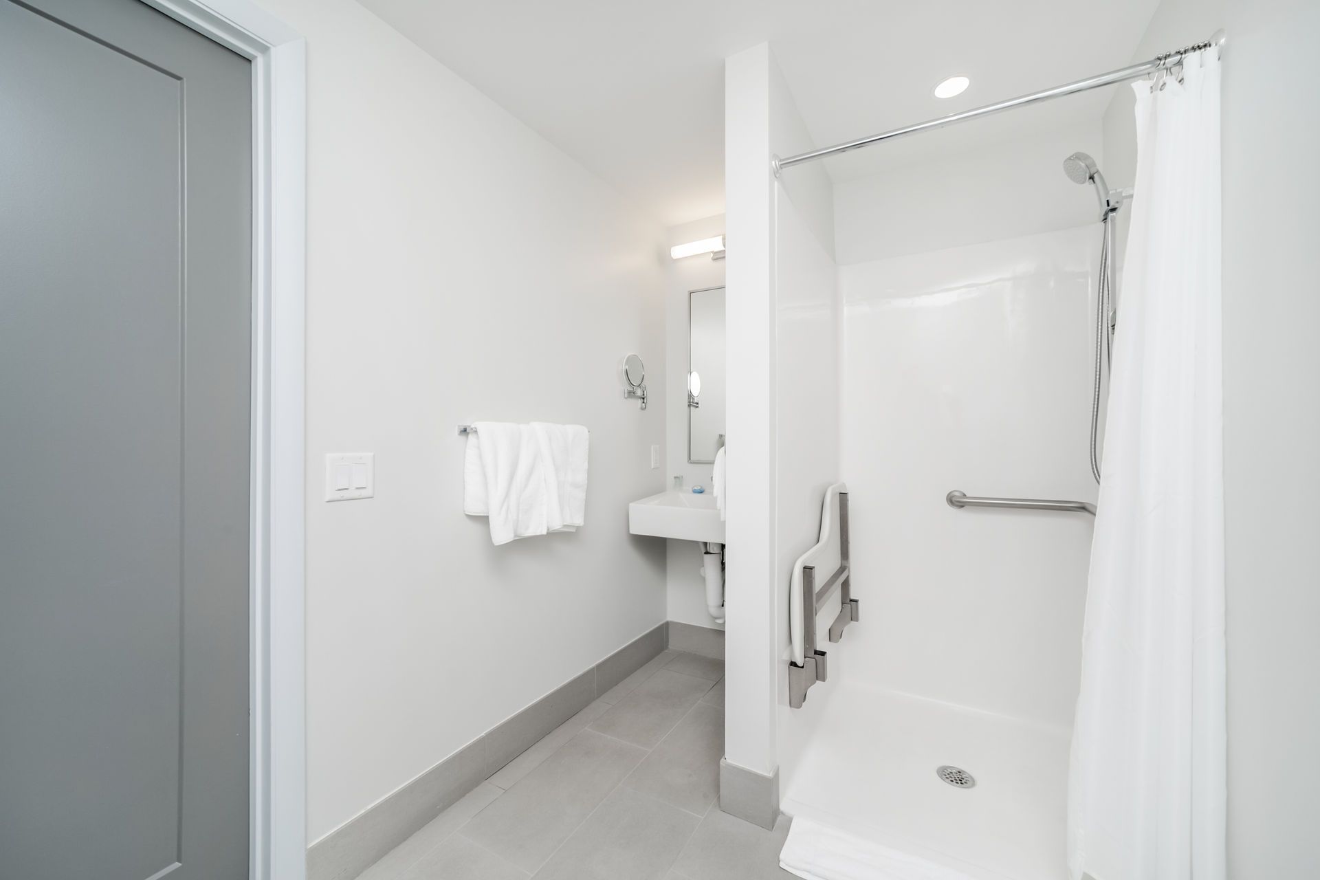 Bright white accessible bathroom with open shower, grab bars, and sink.