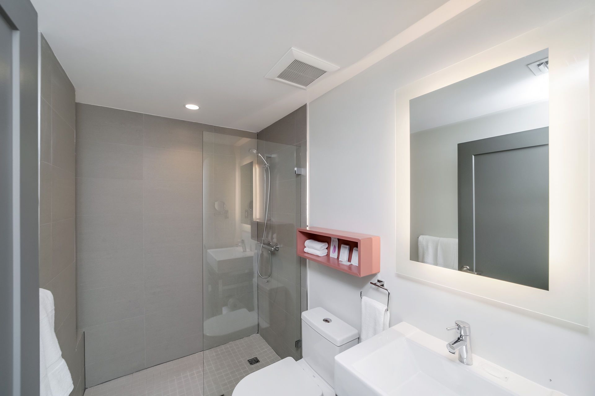 Modern bathroom with a glass shower, white sink, and large mirror with a lighted frame.
