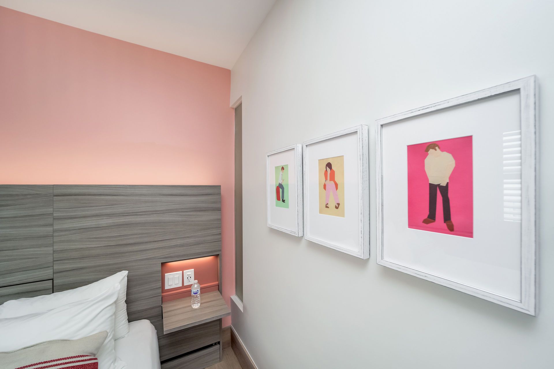 Bedroom corner with bed, nightstand, framed art, and pink/white walls.