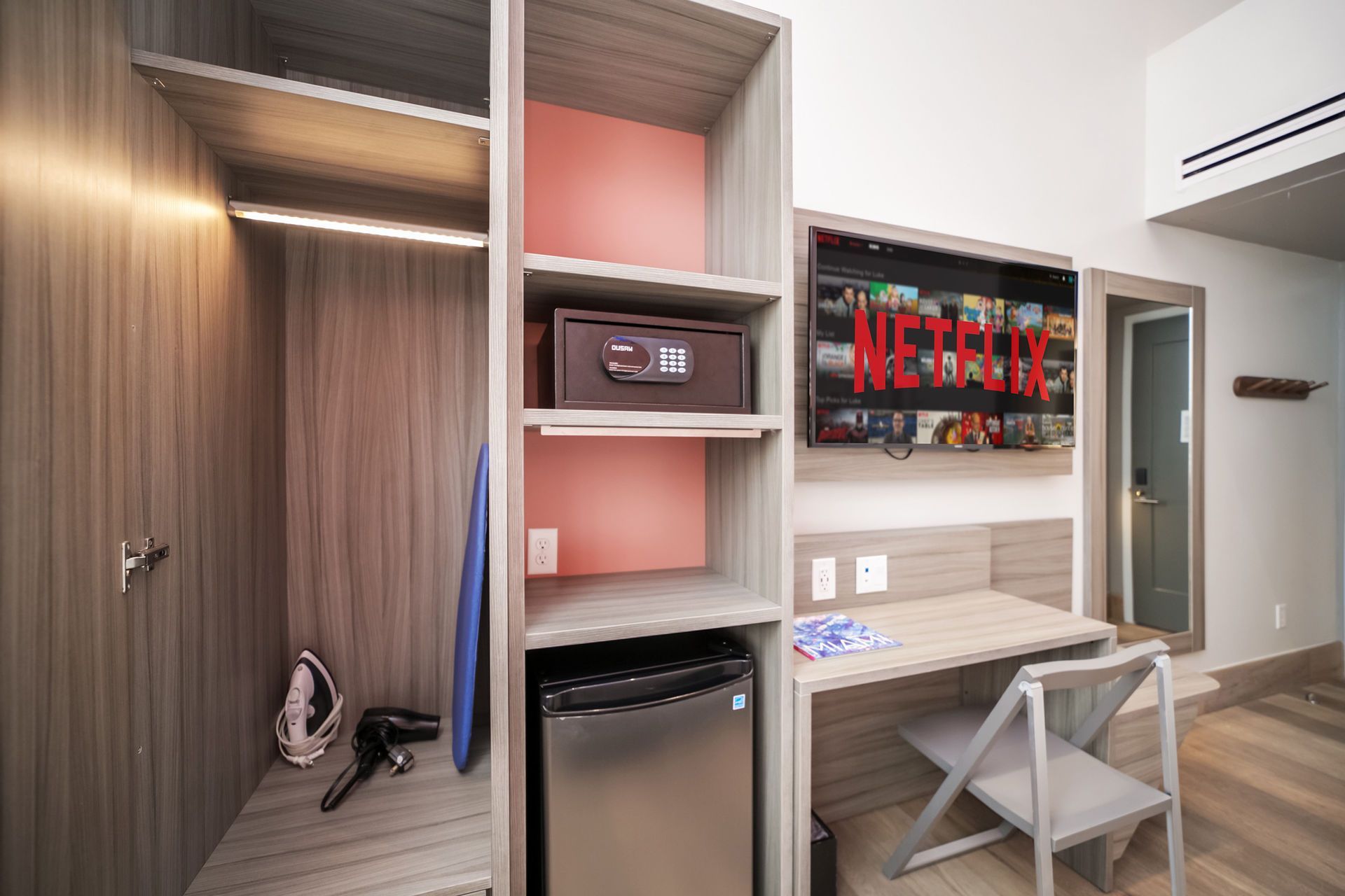 Hotel room with closet, safe, desk, mini-fridge, and TV displaying Netflix.