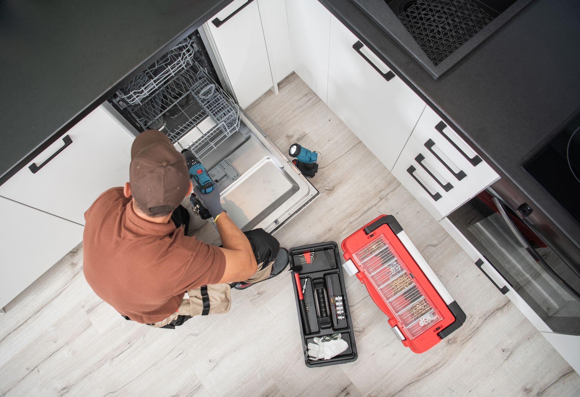 Technician repairing a dishwasher inside a residential apartment kitchen.
