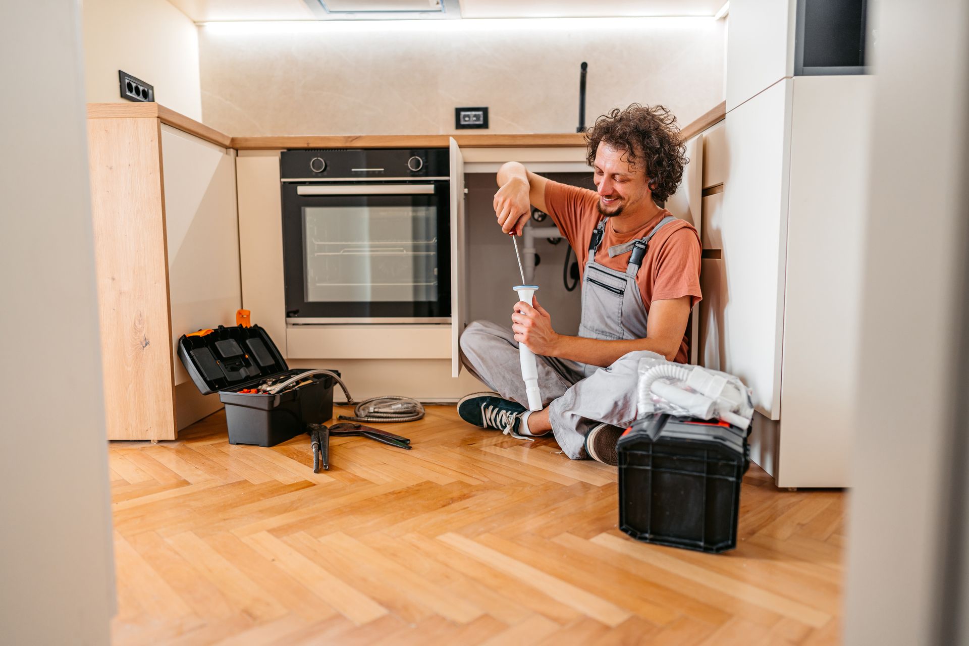 Appliance repair technician fixing kitchen oven with tools on wooden floor.