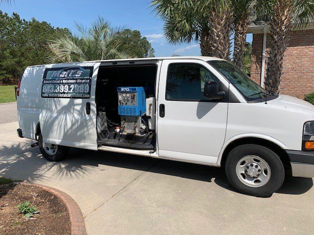 A white van is parked in a driveway with its doors open.
