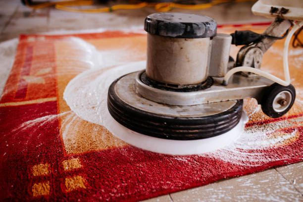 A machine is cleaning a red rug on a tiled floor.