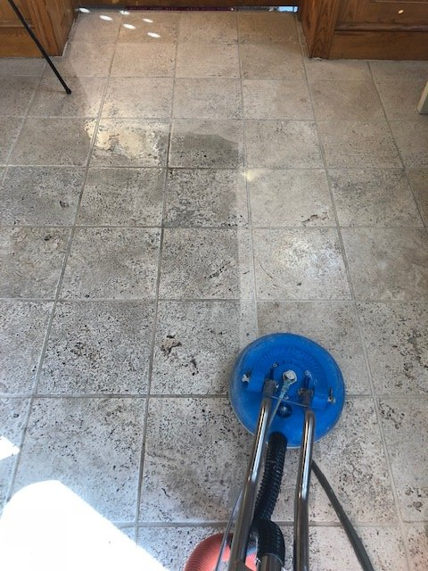 A person is cleaning a tile floor with a vacuum cleaner.
