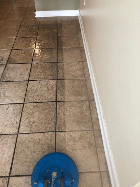 A blue mop is sitting on a tiled floor next to a wall.