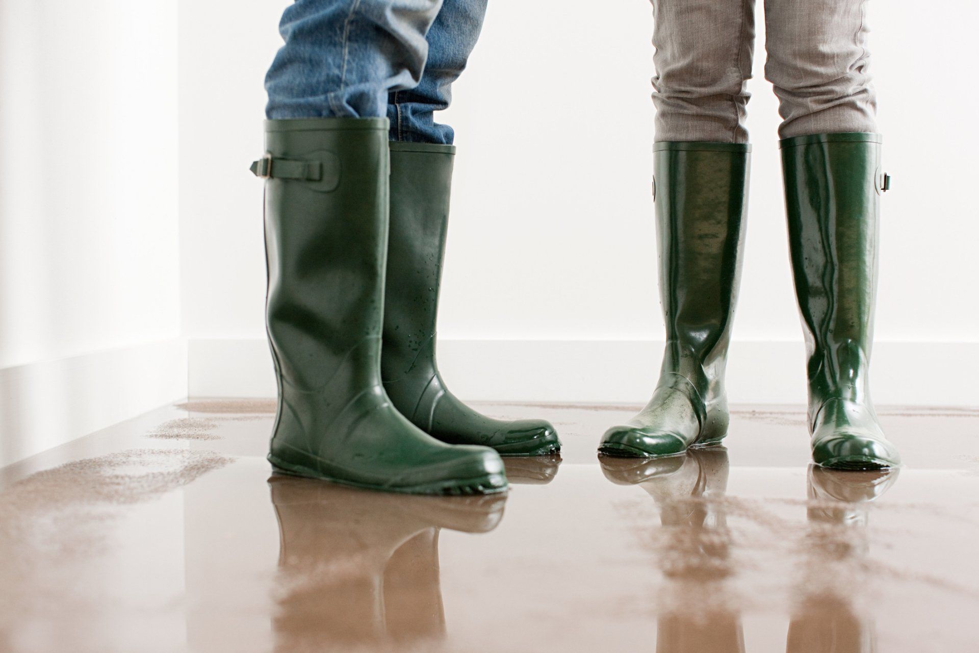 Two people wearing green rain boots are standing in a flooded room.