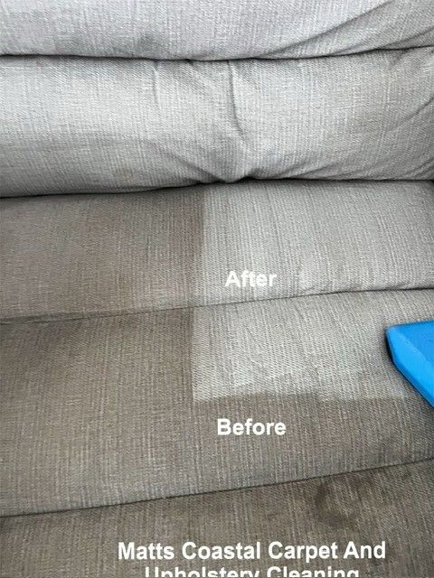 A man is cleaning a couch with a vacuum cleaner.