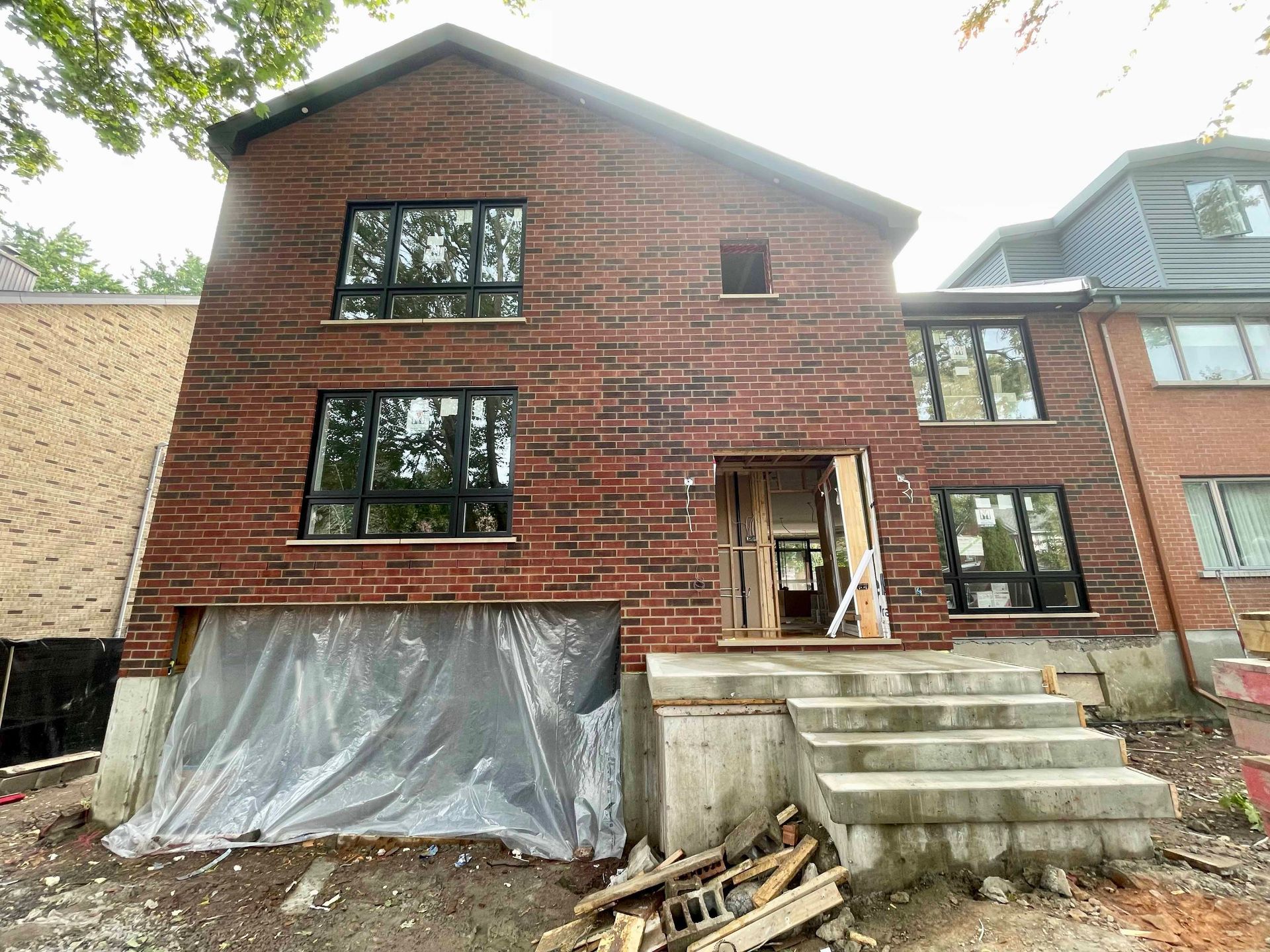 Façade en briques d'un bâtiment en construction, avec des fenêtres à cadre sombre et un escalier en béton.
