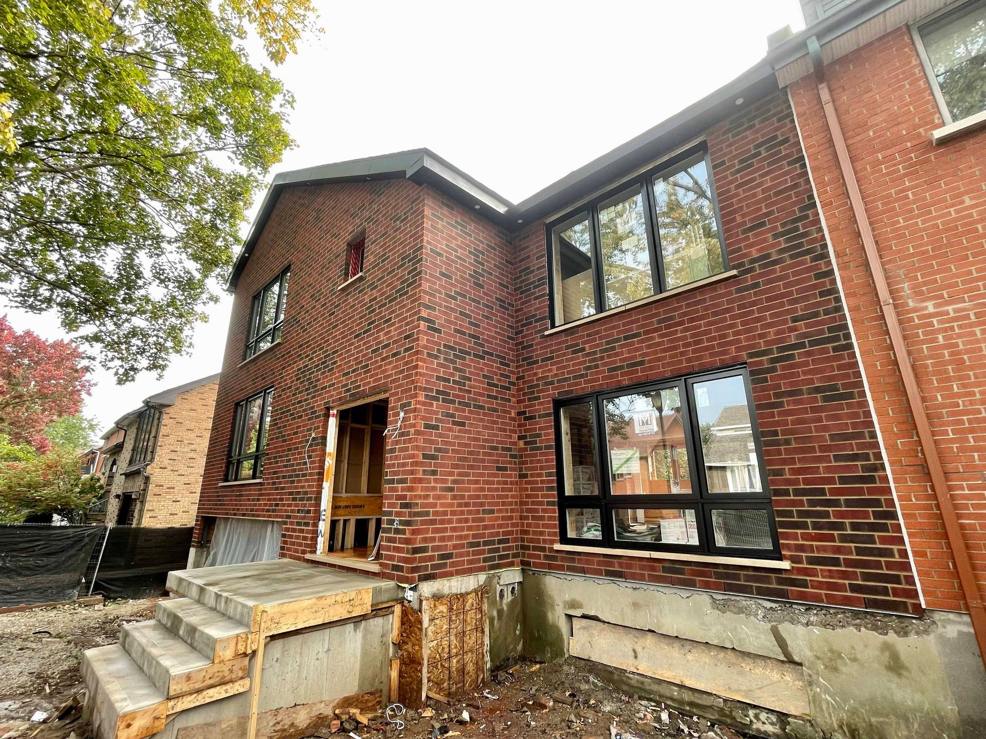 Maison en briques rouges en construction, avec des fenêtres neuves et des marches d'entrée inachevées.