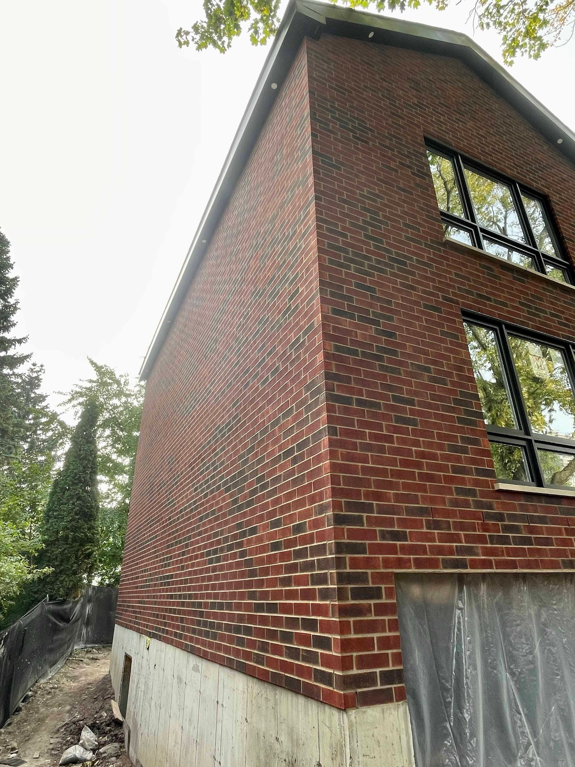 Bâtiment en briques rouges avec un design incurvé sur le côté, des fenêtres noires et des fondations en béton.