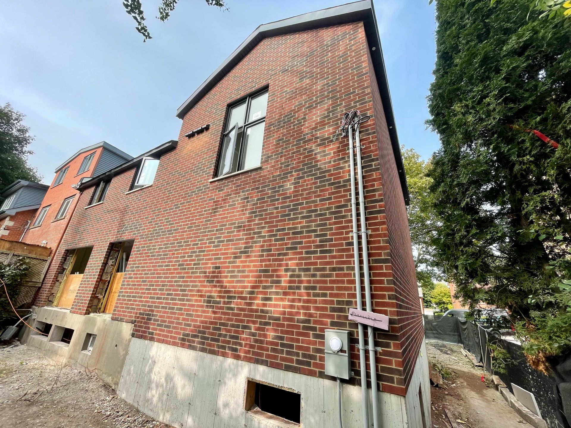 Bâtiment en briques rouges en construction, avec quelques fenêtres et un boîtier électrique.