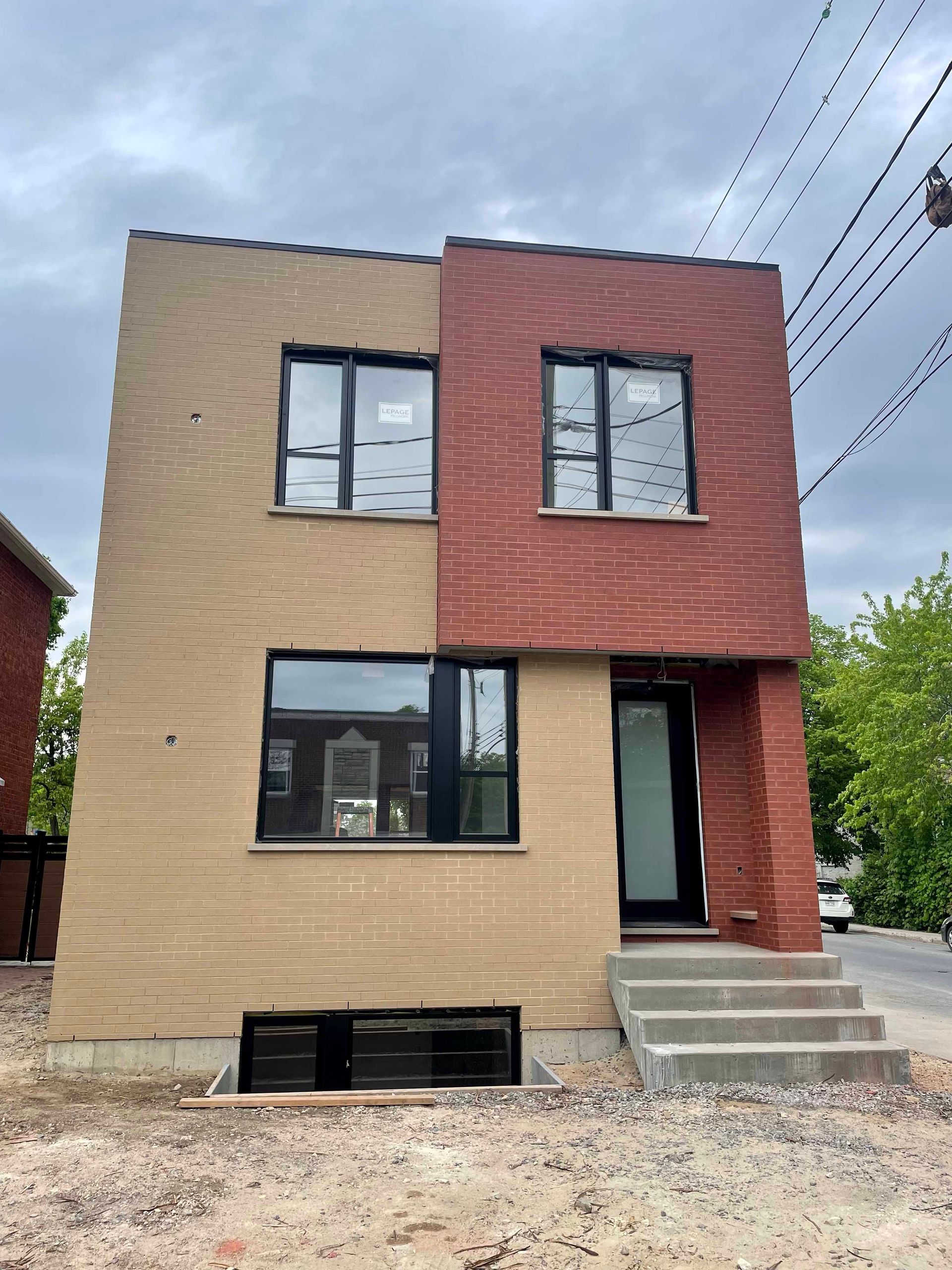Bâtiment en briques de deux étages avec des façades beiges et rouges, des fenêtres à encadrement noir et des marches en béton menant à la porte.