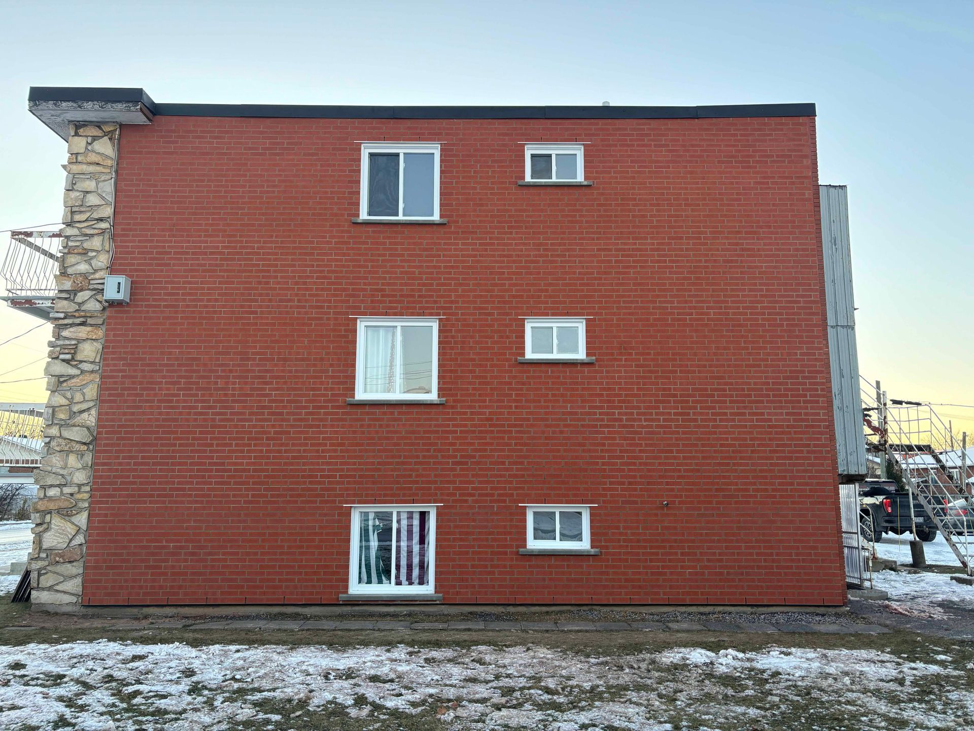 Immeuble d'appartements en briques avec des fenêtres dépareillées et un pilier en pierre. Sol enneigé.
