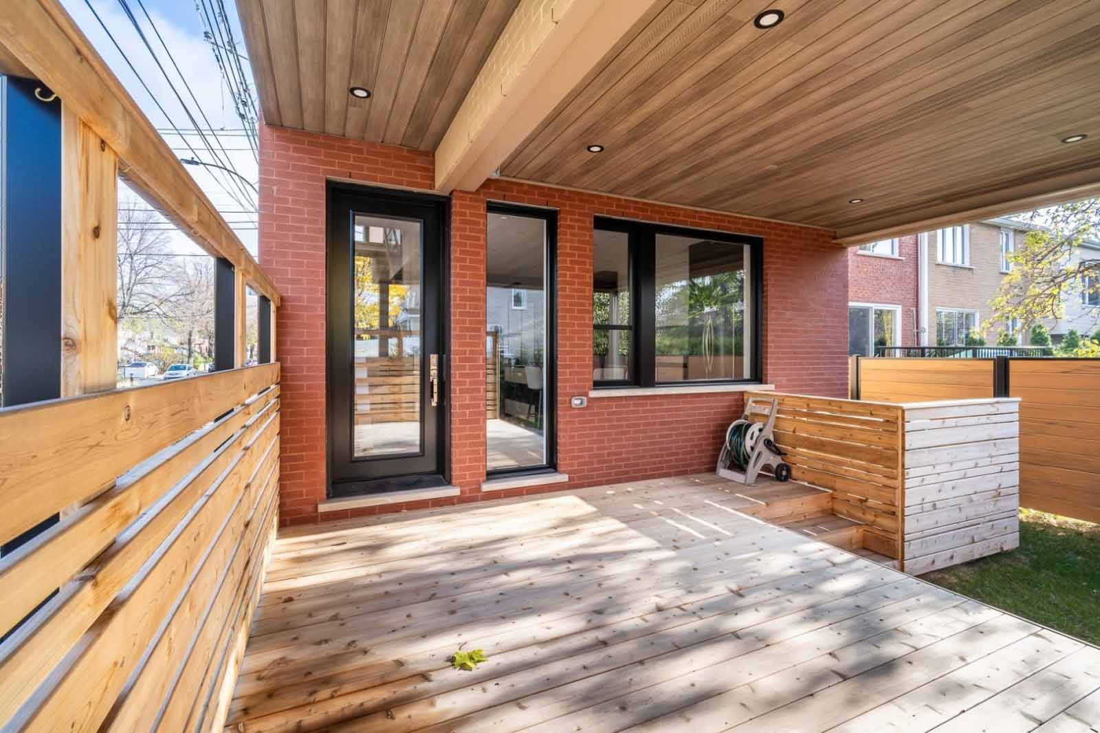 Terrasse en bois avec bâtiment en briques et clôture en bois. Lumière naturelle grâce aux portes et fenêtres vitrées.
