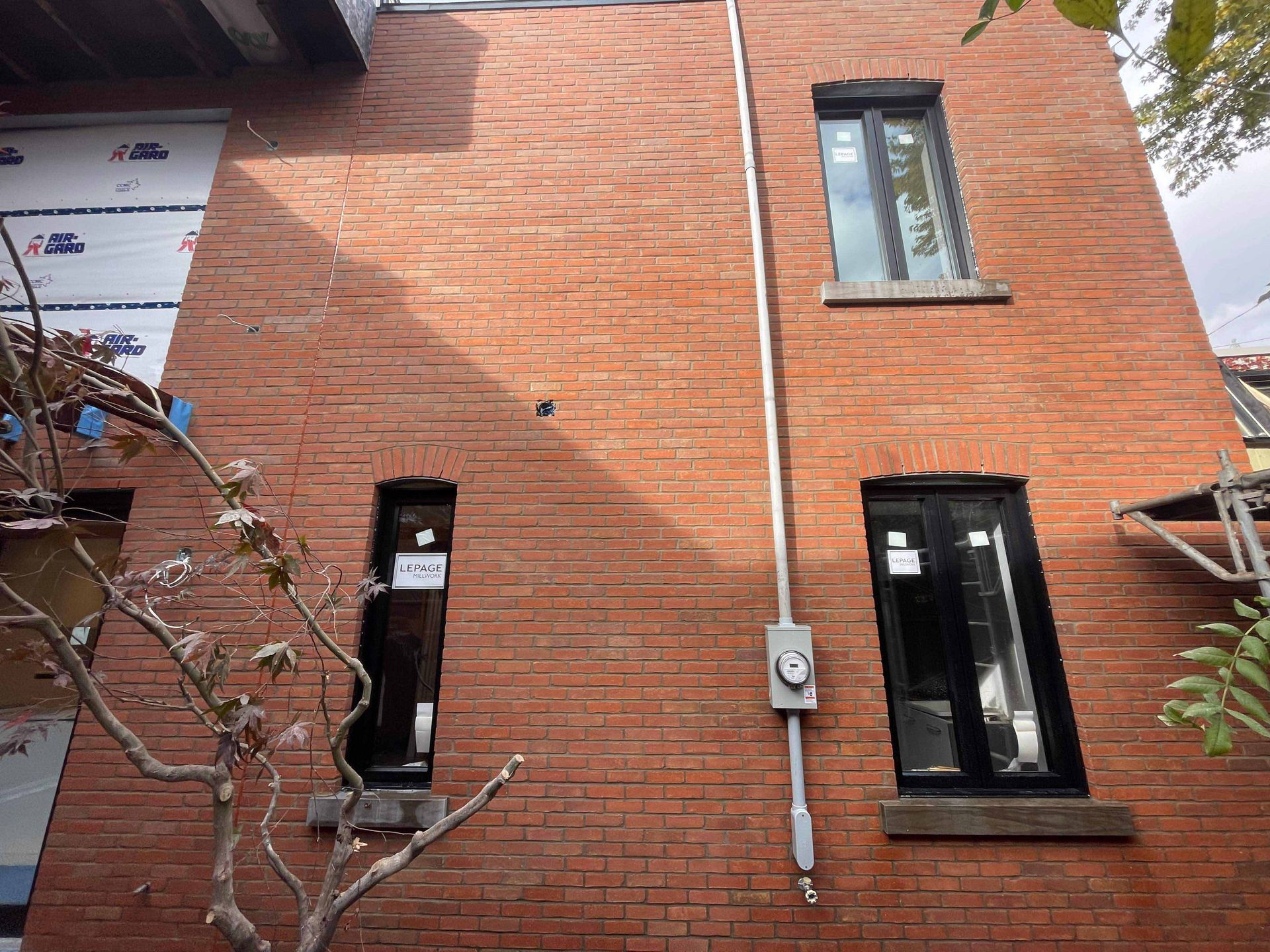 Mur extérieur en briques rouges avec fenêtres, conduits électriques et revêtement apparent.