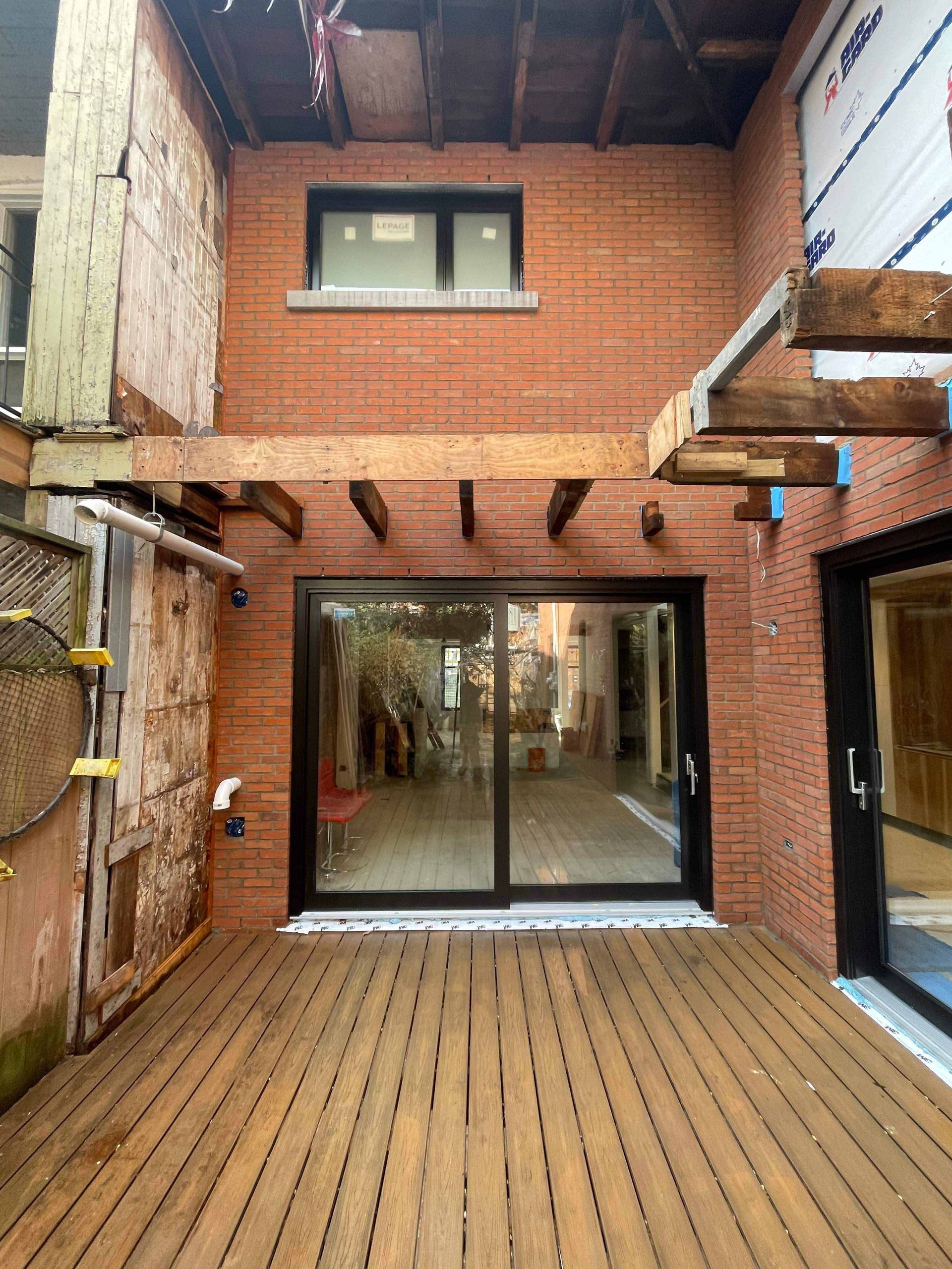 Cour arrière avec terrasse, briques apparentes, grandes portes coulissantes en verre et pergola en bois.