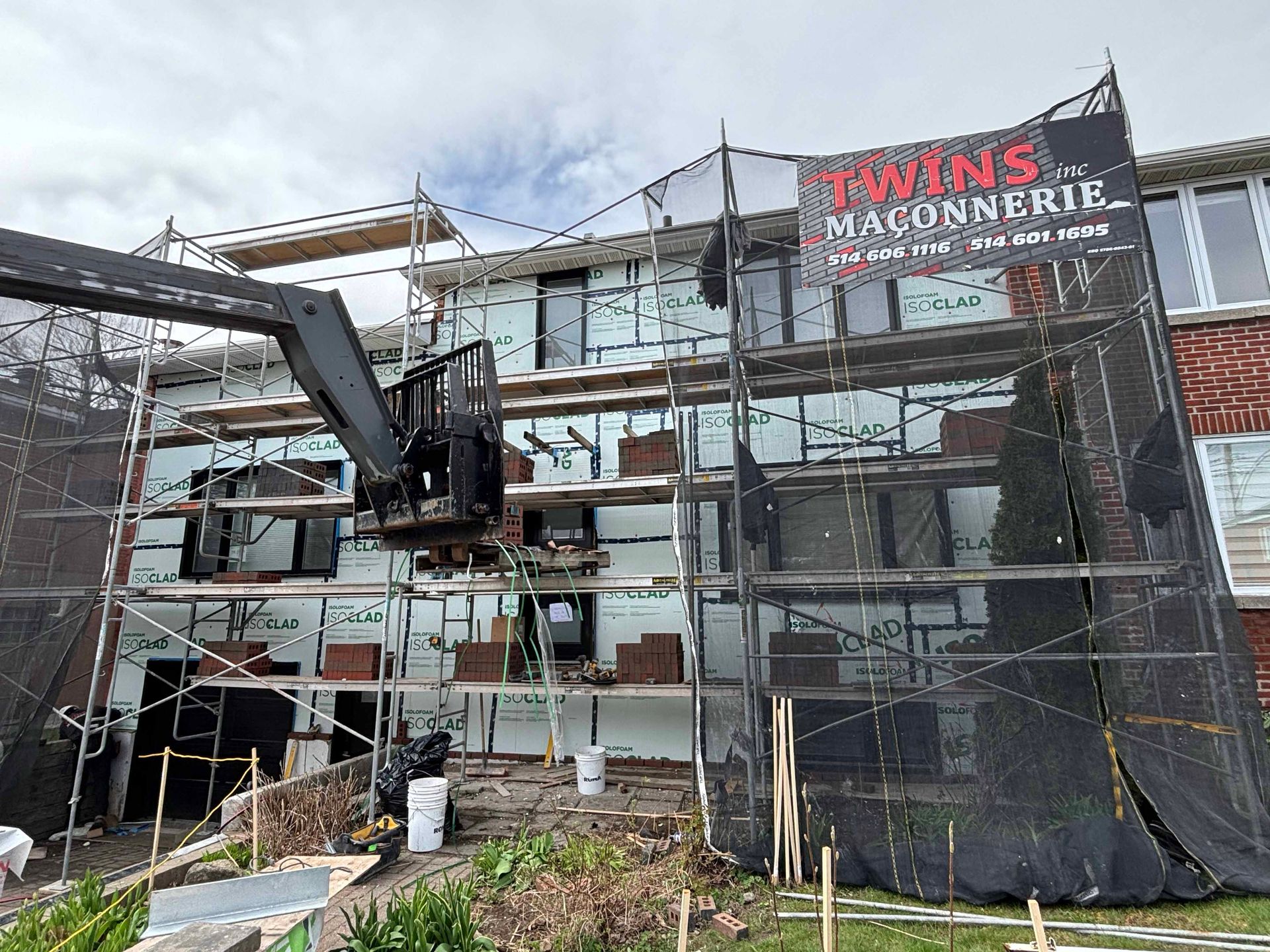 Bâtiment en construction avec échafaudages et maçonnerie ; une grue est visible.