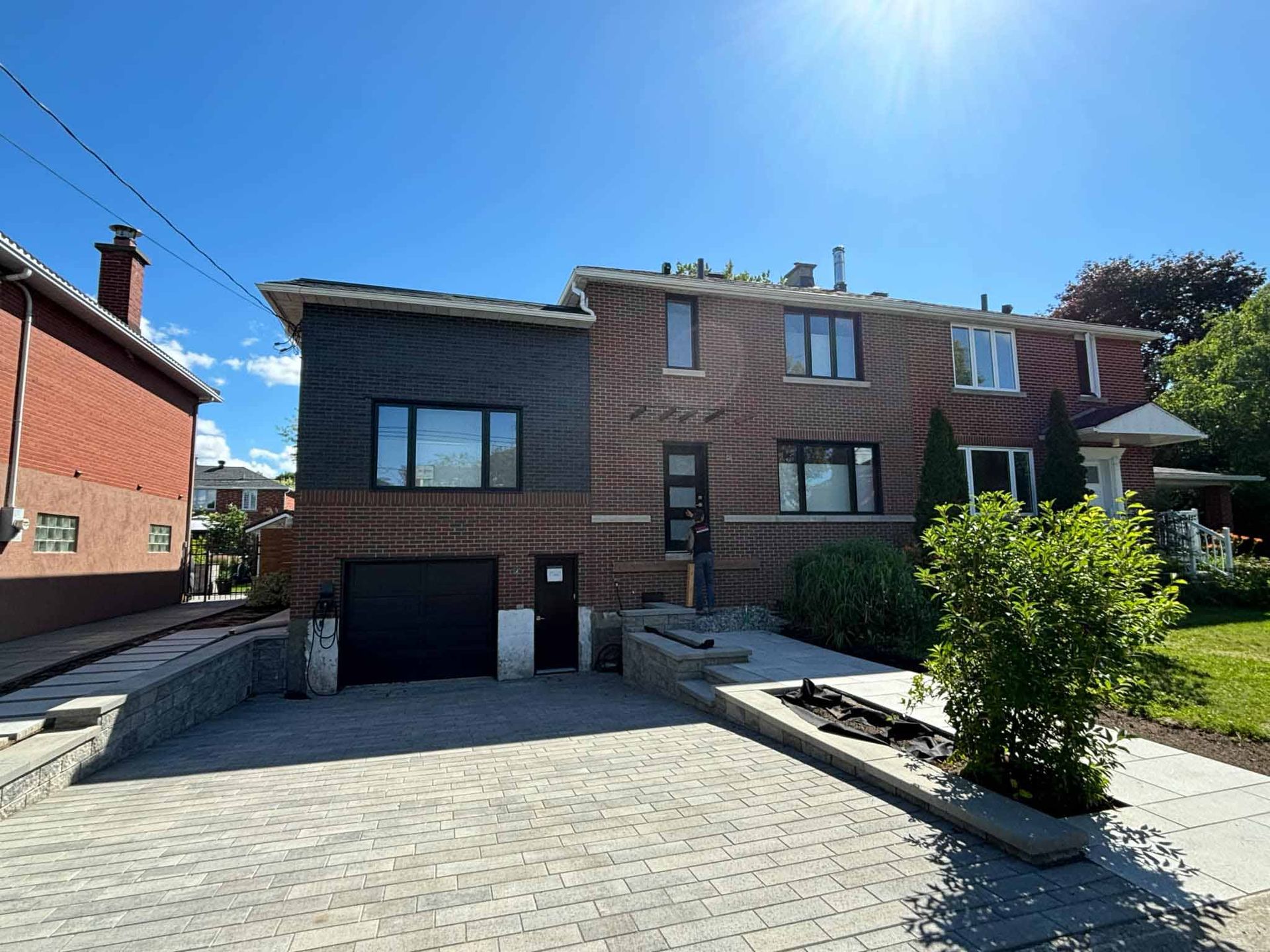 Maison en briques avec garage, allée et aménagement paysager par une journée ensoleillée.