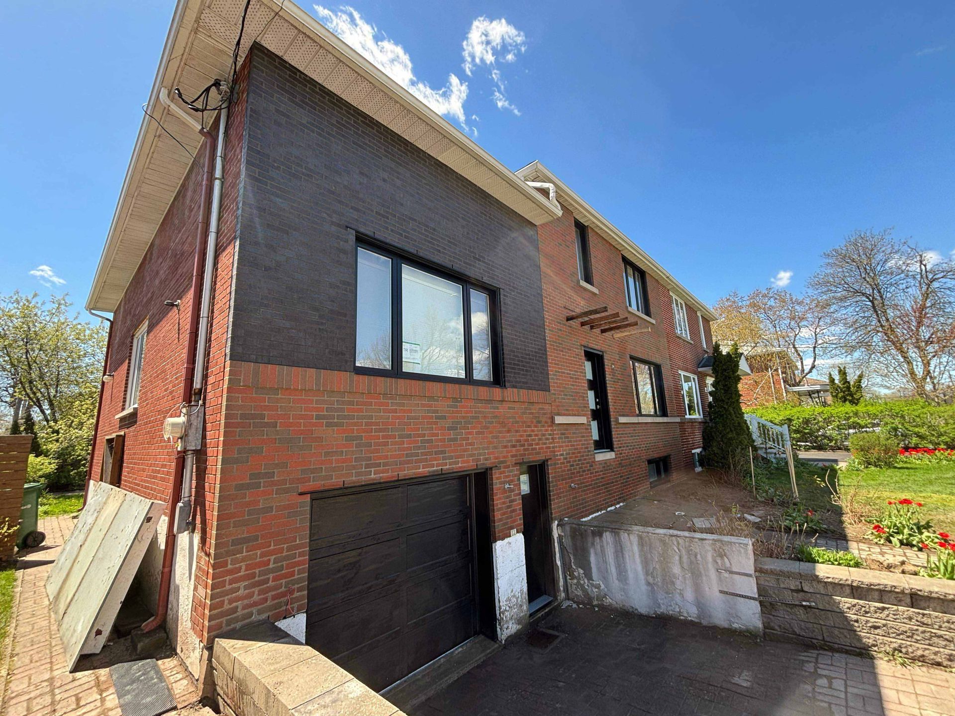Bâtiment en briques avec bardage noir, porte de garage et fenêtres sur fond de ciel bleu.