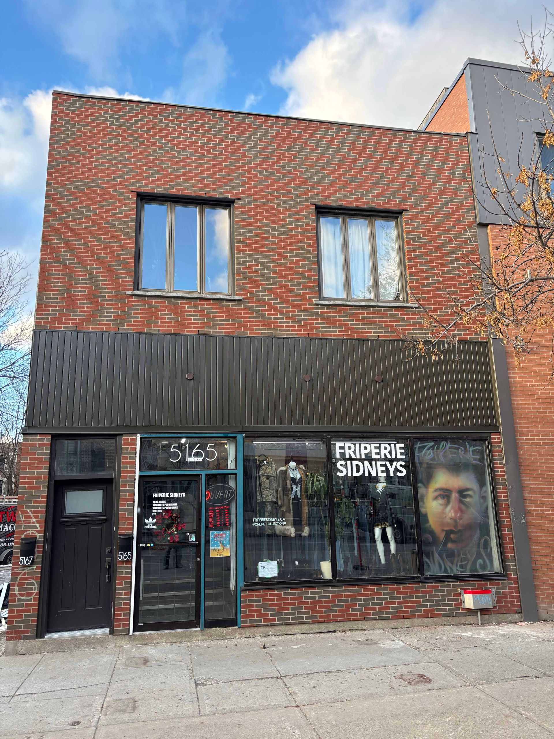 Bâtiment en briques avec vitrine, auvent et porte noire. Enseigne « Freperie Stoney's » en vitrine.